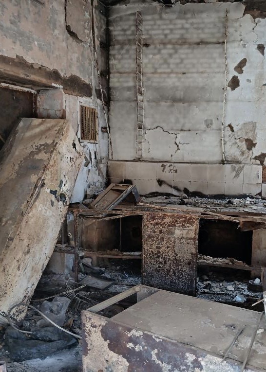 Fire-damaged interior of the family shop, with burnt shelving and debris, before repair
