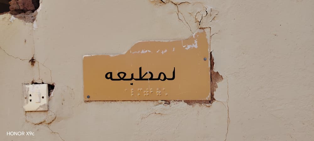 Damaged signage and cracked wall at the Al Noor Institute braille print room, before repair