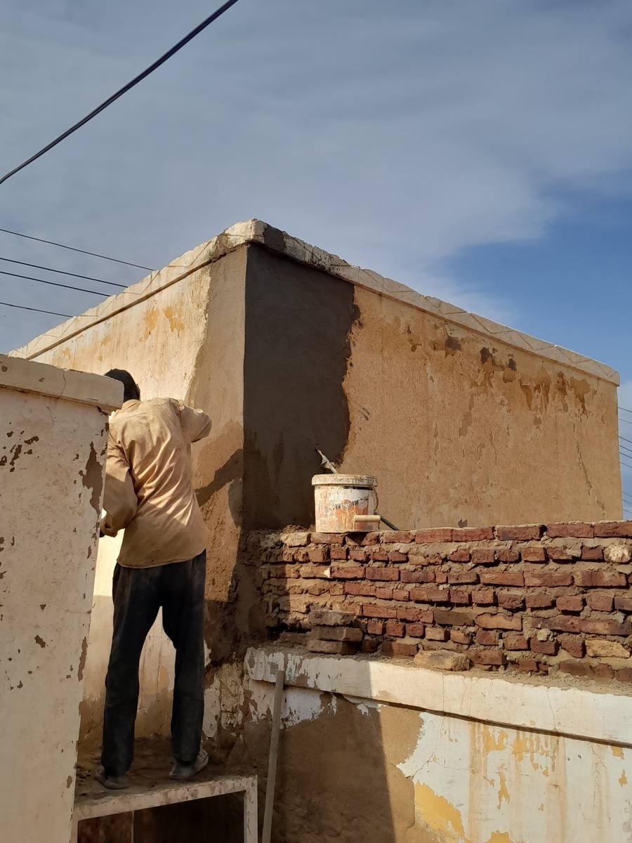 A Sudanese repair worker plastering a rooftop wall
